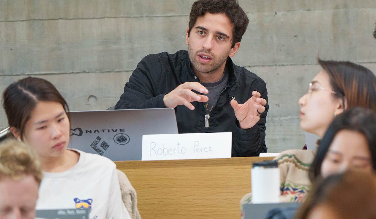 man sitting in classroom gesturing as he speaks