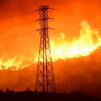 Photo of a wildfire spreading. With a tall electrical tower in the middle of the image.