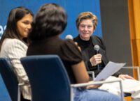 woman speaking with microphone with two students sitting next to her