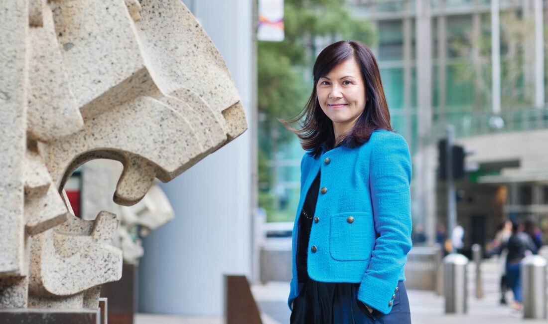 Woman in a blue suit coat standing next to a wall with a lion sculpture in relief jutting out of it.