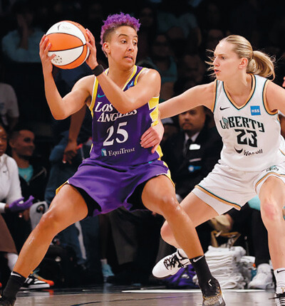 Layshia Clarendon, in a purple Los Angeles Sparks uniform, holding the basketball and being defended by a player for the New York Liberty, in a WNBA game. Photo: Bruce Bennett/Getty Images.