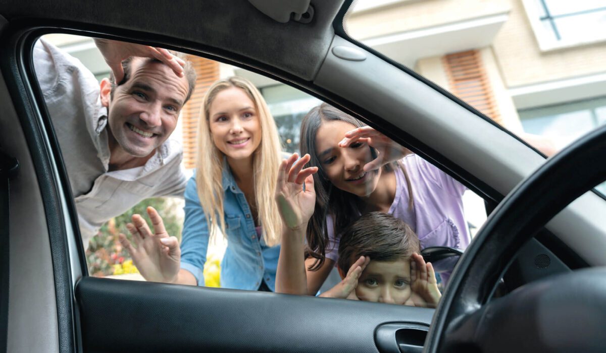 A man, women, and two children looking into a car window and smiling.