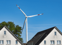 Photo of an energy windmill in the middle of two white houses.