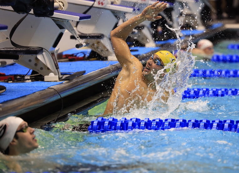 swimmer lifting his arm to cheer in the pool wearing goggles and a cap