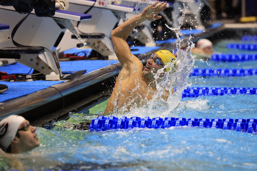 Man wearing goggles and swim cap with arm stretched up in swimming pool during competition