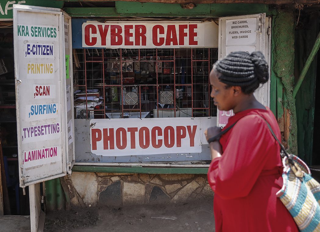 A woman wearing red walks past an internet cafe in the Kibera neighborhood of Nairobi, Kenya.