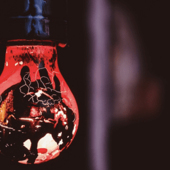 Photo of a red-gold (ish) light bulb with designs on it, in front of dark backdrop.