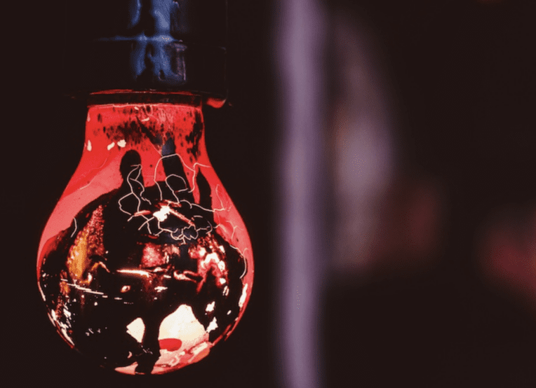 Photo of a red-gold (ish) light bulb with designs on it, in front of dark backdrop.