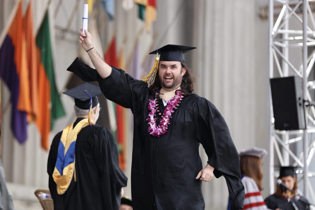 graduate walking the stage with his diploma in cap and gown