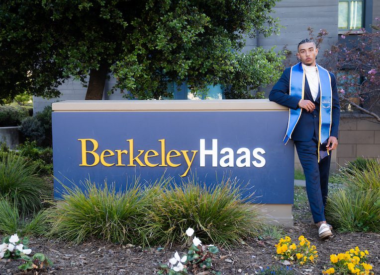 man wearing commencement sash standing next to Berkeley Haas sign