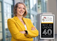 A smiling woman with short blond wears a yellow blazer and stands with arms crossed. A badge reads: Poets&Quants Best 40 Under 40 Professors