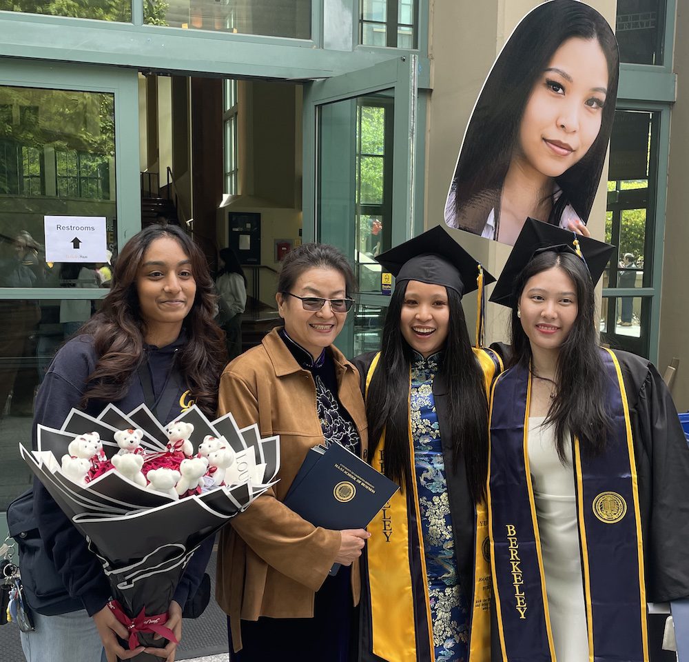 four women, two wearing commencement cap and gowns