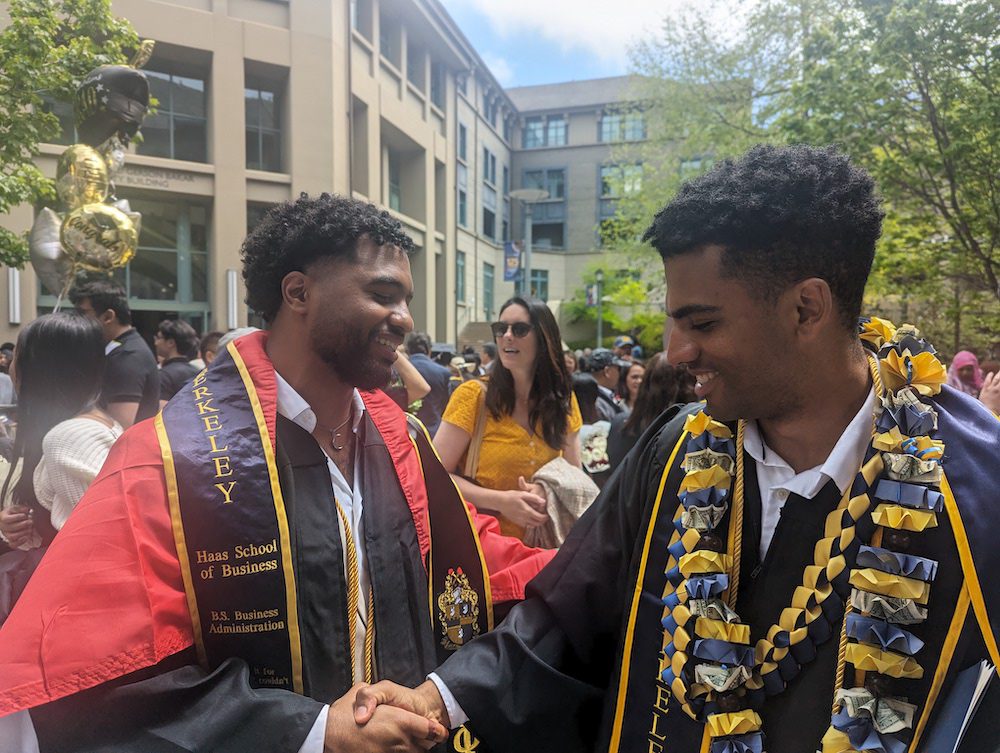 two men in graduation cap and gowns shaking hands