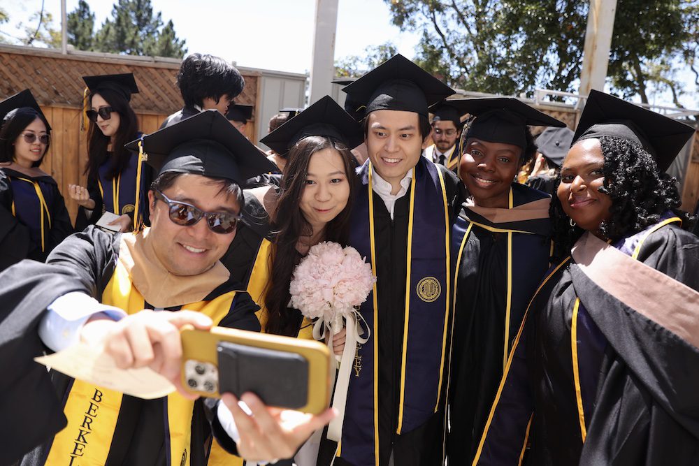 group of graduates in caps and gowns, one taking a selfie