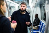 Portrait of young bearded man holding a smartphone and talking with young woman while traveling by subway