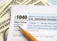 Photo of dollar bills, an IRS 1040 form and a pencil.