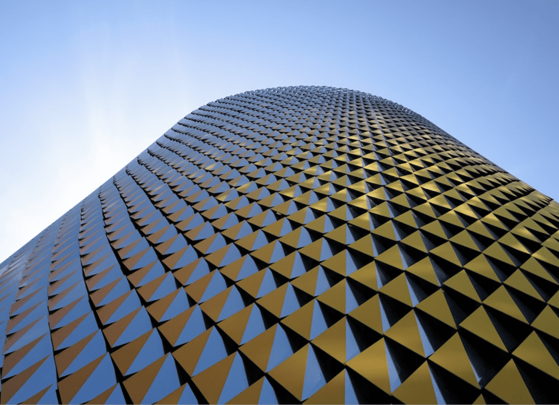 Photo of an abstract building. Looks like a hundreds of small bronze triangles put together to create a building.