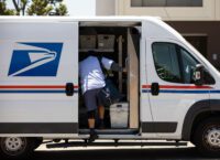 A US Postal Service mail carrier climbs carrying mail climbs into a delivery van.