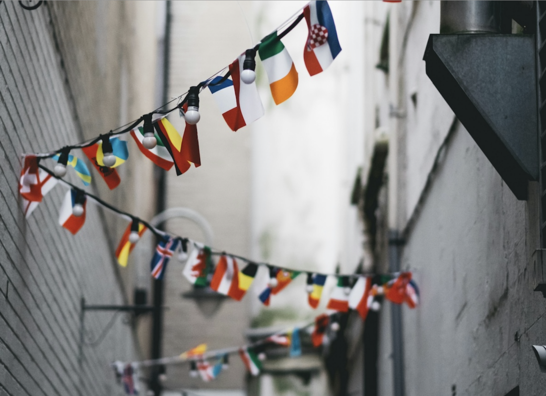 A photo of small country flags hanging from a string of lights on in an alley.