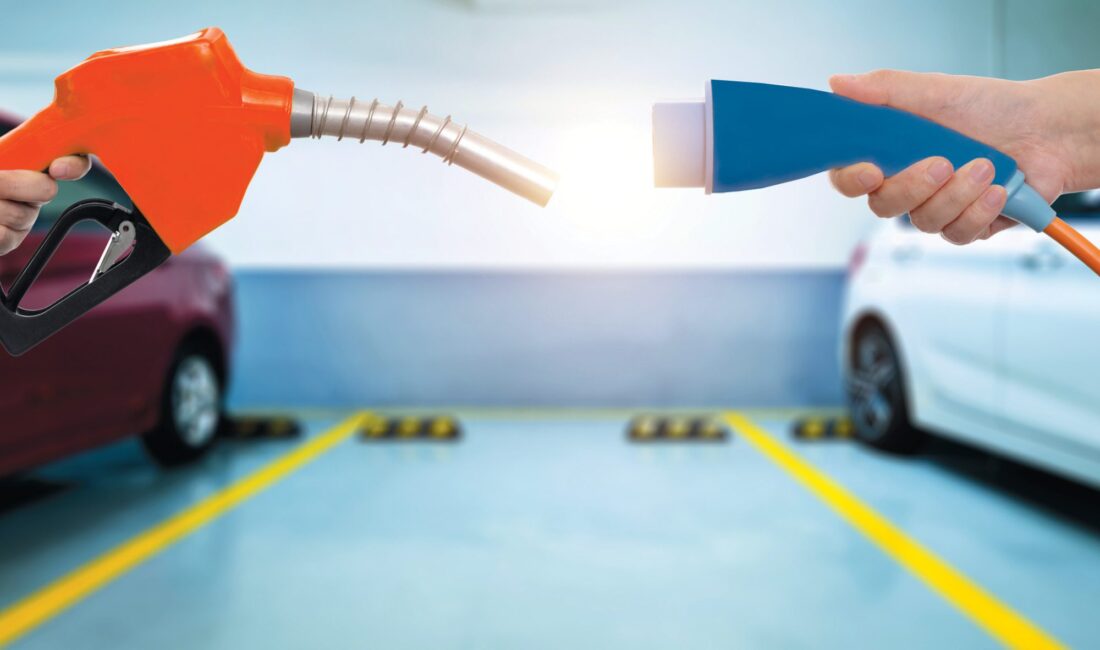 The red handle of a gas pump and blue charging cord for an electric vehicle.