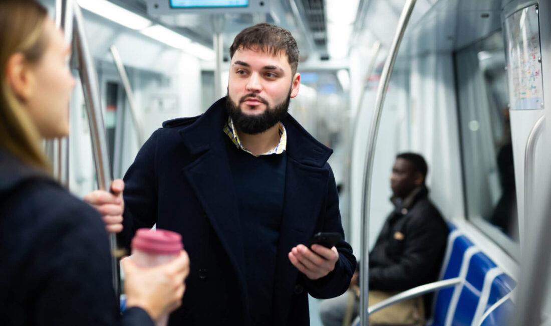 Portrait of young bearded man holding a smartphone and talking with young woman while traveling by subway.