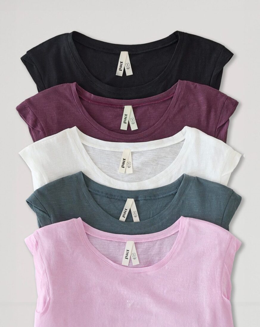 Image of 5 Pact t-shirts in different colors laid flat on a light background