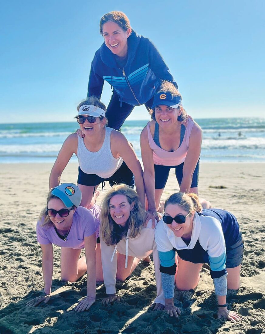 Six women build a pyramid on the beach.