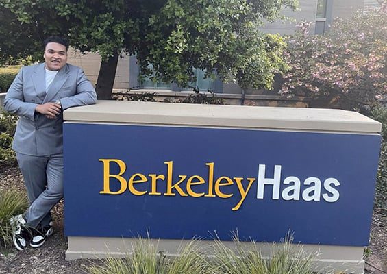 man in suit leaning into Haas sign on campus