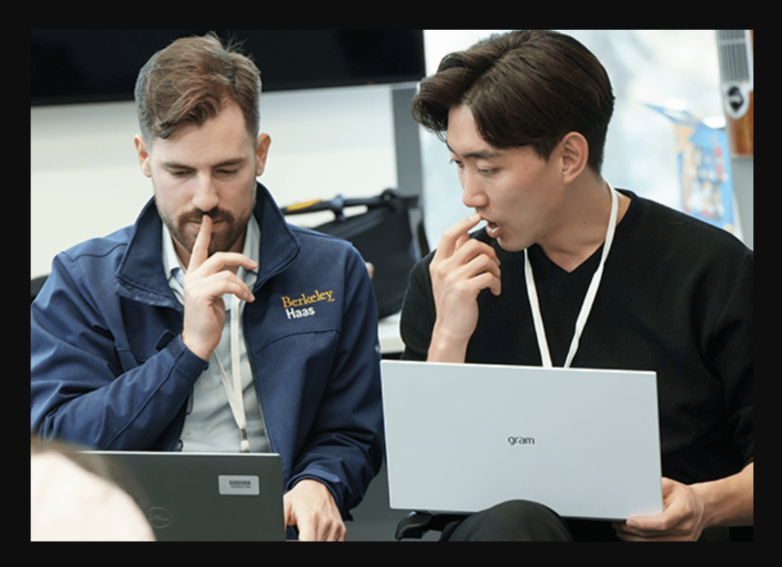 Photo of two MBA male students talking with their laptops on their laps.