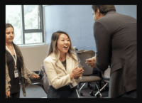 A woman and a man engaged in a conversation. Hands clasped together. Woman smiling. Man's back to camera.