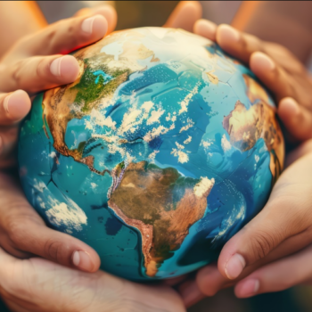 Photo of different hands (people of different races) holding onto a small replica of Earth.