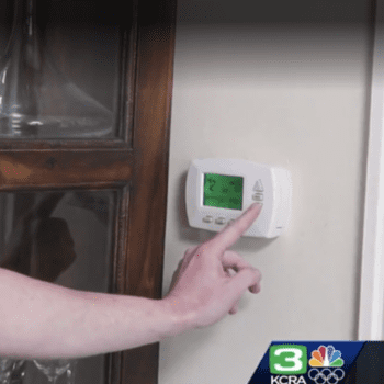 Screengrab of a photo of a hand touching/adjusting a thermostat.