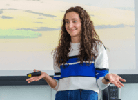 Woman presenting in front of class smiling.