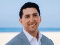 Photo of Chris Murray, MBA 25. White male, wearing a white collar top, blue blazer. Smiling against natural sand and beach backdrop.