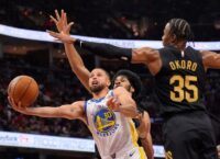 Golden State Warriors guard Stephen Curry reaches out with the basketball in front of Cleveland Cavaliers center Jarrett Allen, rear, and forward Isaac Okoro in the first half of an NBA basketball game.