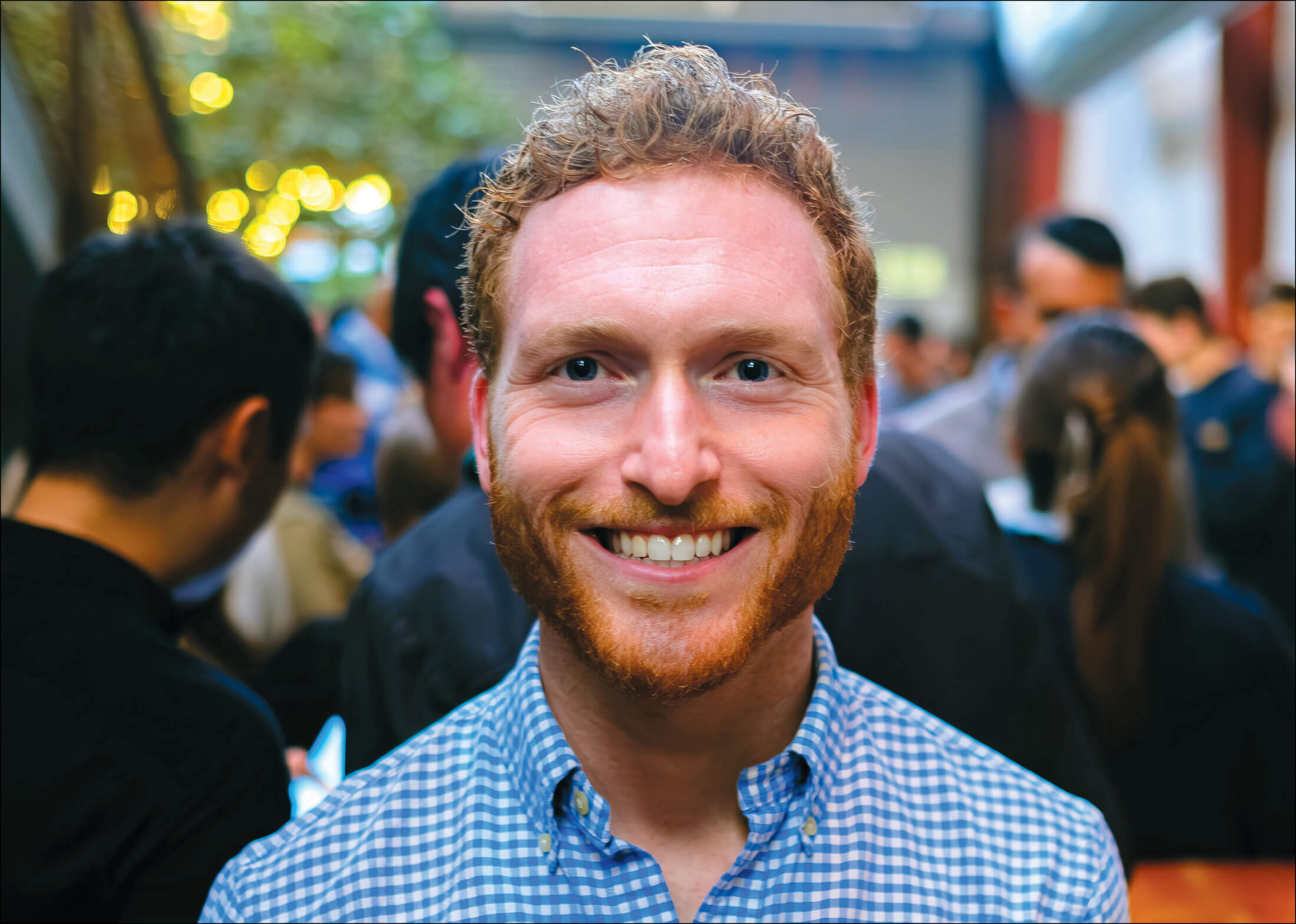 Person with red hair and beard wearing a blue and white checked shirt smiling