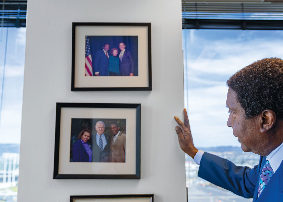 Person in a blue suit coat and tie looks at two framed photos on a column between two windows