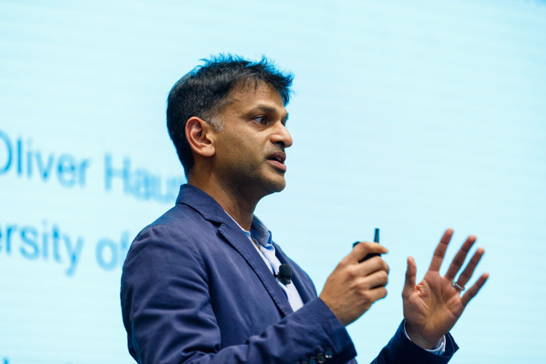 A man in wearing a suit is speaking, gesturing with his hands