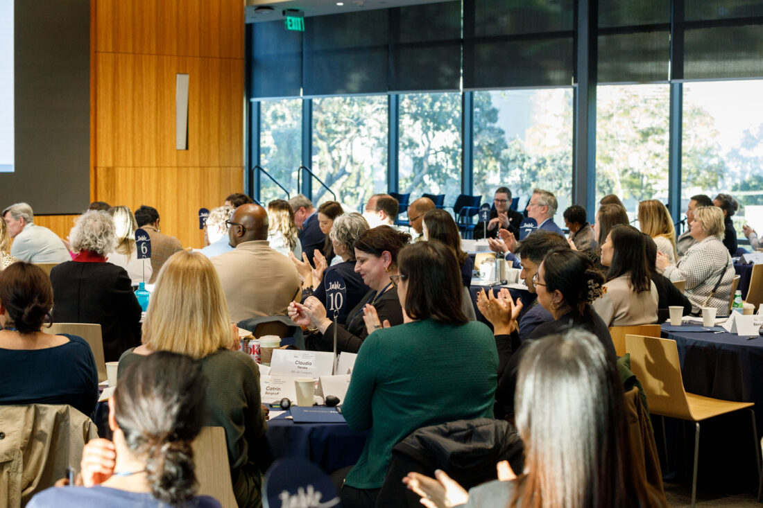 A crowded room of people sitting at tables and applauding