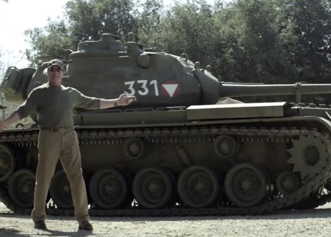 Man with arms wide open posing in front of army tank vehicle.