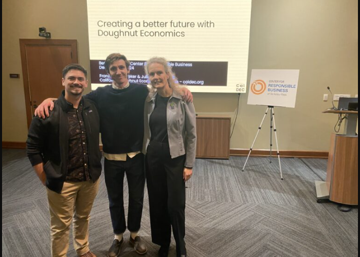 Photo of 3 people posing in front of Doughnut Economics Powerpoint screen in the Wells Fargo room.